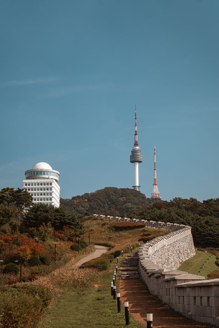 Namsan Tower in Seoul surrounded by lush greenery and historic walls during fall season.